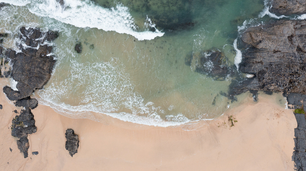 Aerial view of Harlyn Bay Beach with turquoise water white waves crashing against dark rocks and golden sand Saint Merryn Cornwall United Kingdom.