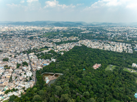Aerial view of the urban landscape of Udaipur featuring a dense city area bordering a large lush green forest park and a small pond in Udaipur Rajasthan India. Aerial view of the urban landscape of Udaipur featuring a dense city area bordering a large lush green forest park and a small pond in Udaipur Rajasthan India.