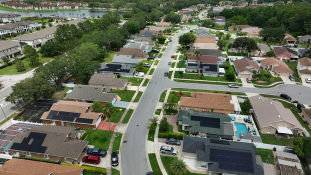Aerial view of a suburban residential neighborhood featuring houses with solar panels swimming pools and lush green trees in Orlando Florida United States.