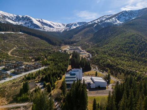 Aerial view of the Demanovska Dolina valley with snow capped mountain peaks dense evergreen forests and modern hotel buildings under a clear blue sky in Demanovska Dolina Zilina Region Slovakia.