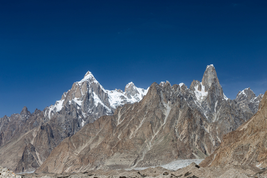 View of the majestic snow capped peaks and rugged rocky slopes of the Baltoro Glacier under a clear blue sky in Baltoro Gilgit Baltistan Pakistan.