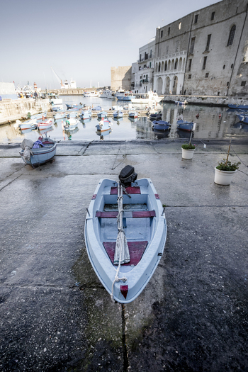 View of a small blue boat on a concrete ramp overlooking a harbor filled with traditional fishing boats and historic stone buildings in Polignano a Mare Apulia Italy.