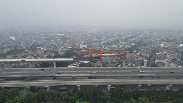 Aerial view of a large orange gantry crane installing a concrete segment on an elevated highway construction site above a busy road in an urban area of Bekasi Barat West Java Indonesia. Aerial view of a large orange gantry crane installing a concrete segment on an elevated highway construction site above a busy road in an urban area of Bekasi Barat West Java Indonesia.