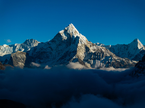 Aerial view of the snow capped peak of Ama Dablam rising above a sea of clouds under a clear blue sky in Nepal.
