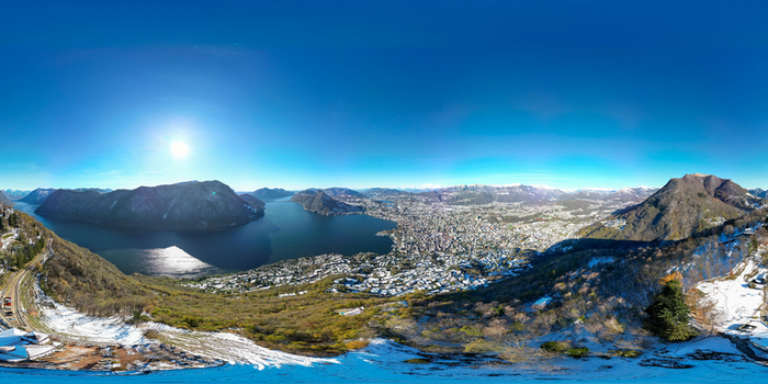 Aerial view of Lake Lugano and the city surrounded by snow dusted mountains with sun reflecting on the water Lugano Ticino Switzerland.