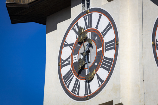 View of the vibrant clock tower stands tall against the bright blue sky its golden hands a stark contrast to the white stone Graz Styria Austria. View of the vibrant clock tower stands tall against the bright blue sky its golden hands a stark contrast to the white stone Graz Styria Austria.