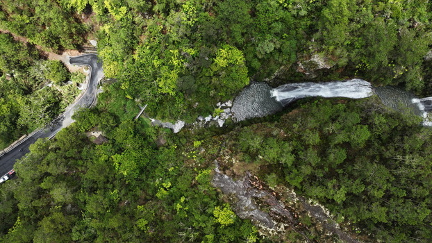 Aerial view of Salto de Aguas Blancas waterfall surrounded by lush green forest and a winding mountain road in Constanza La Vega Province Dominican Republic.