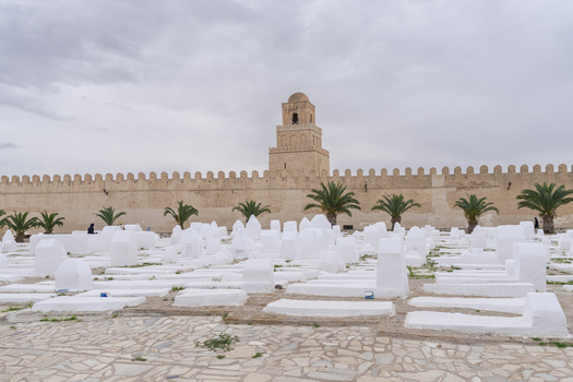 View of the Great Mosque of Kairouan with its iconic minaret rising above a historic cemetery filled with white washed tombs in Kairouan Kairouan Governorate Tunisia.