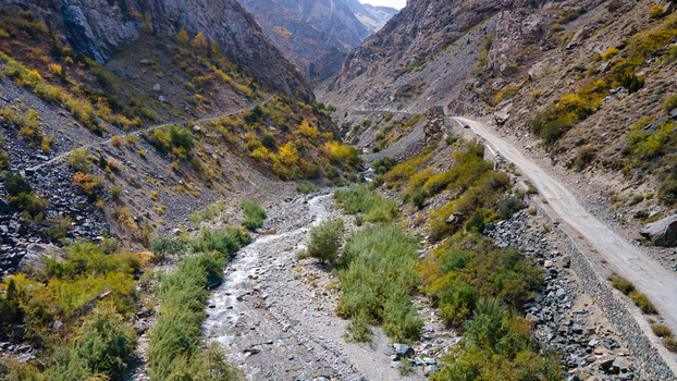 Aerial view of the rugged landscape near Deosai Top featuring a winding river through a rocky valley with a dirt road along the slope Skardu Gilgit Pakistan.