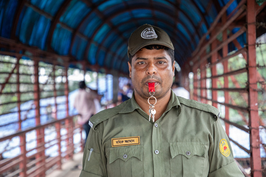 Dhaka Bangladesh 15 June 2018 View of a security guard in green uniform blowing a red whistle on a covered pedestrian bridge at Airport Railway Station. Dhaka Bangladesh 15 June 2018 View of a security guard in green uniform blowing a red whistle on a covered pedestrian bridge at Airport Railway Station.