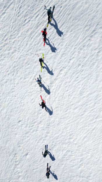 Aerial view of Pointe Ronde with a group of skiers climbing a steep snow covered mountain slope in single file Trient Valais Switzerland.