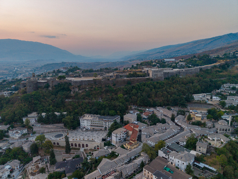 Aerial view of Gjirokaster Fortress overlooking the historic stone city with traditional slate roofed houses and lush hills in Gjirokaster Gjirokaster County Albania. Aerial view of Gjirokaster Fortress overlooking the historic stone city with traditional slate roofed houses and lush hills in Gjirokaster Gjirokaster County Albania.