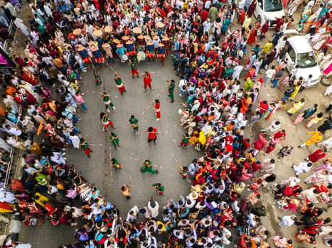Dhaka Bangladesh 13 April 2026 Aerial view of a vibrant street performance with red and green costumed figures amid a dense colorful crowd on grey pavement.