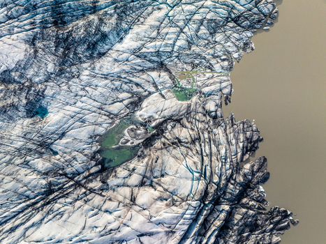 Aerial view of a glacier with deep crevasses intricate ice patterns and vibrant meltwater pools meeting the sediment rich water along the coast of Iceland. Aerial view of a glacier with deep crevasses intricate ice patterns and vibrant meltwater pools meeting the sediment rich water along the coast of Iceland.