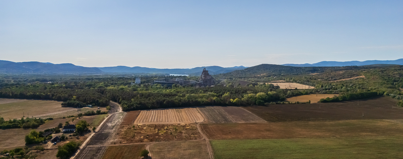 Aerial view of a cement factory and silos amid farmland forest and low hills near Vac Hungary with the Danube River visible beyond the industrial complex. Aerial view of a cement factory and silos amid farmland forest and low hills near Vac Hungary with the Danube River visible beyond the industrial complex.