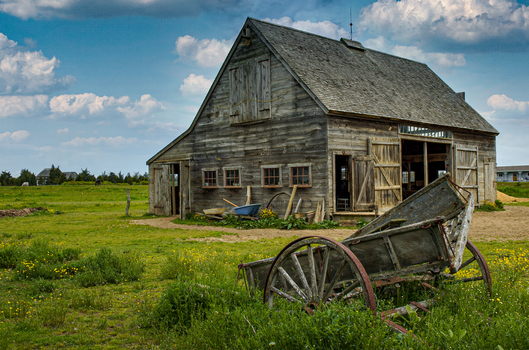 View of a rustic weathered wooden barn and an old cart in a green field under a cloudy sky in Edgartown Massachusetts United States.