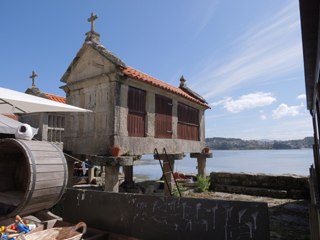 View of a traditional stone horreo with wooden doors and a cross on top situated along the coastal waterfront in Combarro Pontevedra Spain.