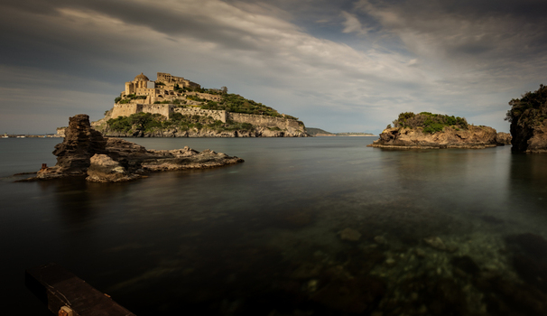 View of the historic Aragonese Castle on its rocky islet surrounded by calm sea waters under a cloudy sky Ischia Campania Italy. View of the historic Aragonese Castle on its rocky islet surrounded by calm sea waters under a cloudy sky Ischia Campania Italy.