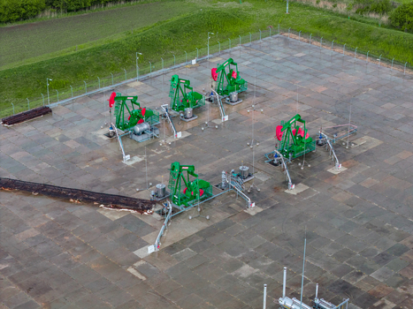 Aerial view of several green oil pumpjacks operating on a paved industrial site surrounded by green fields in Nasedlovice South Moravian Region Czechia.