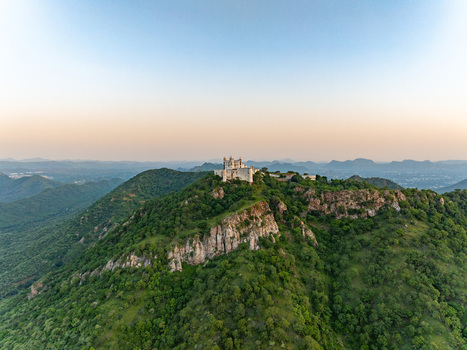 Aerial view of the historic Sajjangarh Monsoon Palace perched on a lush green hilltop overlooking the surrounding Aravalli hills in Udaipur Rajasthan India.