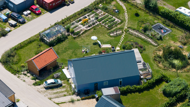 Aerial view of Ecodorp Bolderburen featuring a blue house a vegetable garden a greenhouse and a wooden shed in a sustainable community setting Almere Flevoland Netherlands. Aerial view of Ecodorp Bolderburen featuring a blue house a vegetable garden a greenhouse and a wooden shed in a sustainable community setting Almere Flevoland Netherlands.