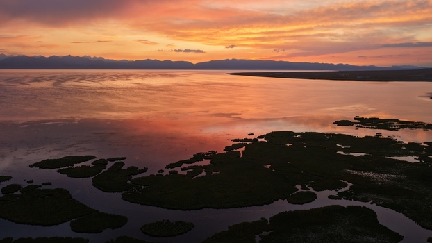 Aerial view of Song Kul lake during a vibrant sunset with golden light reflecting on the water and silhouettes of mountains in the distance Naryn Region Kyrgyzstan. Aerial view of Song Kul lake during a vibrant sunset with golden light reflecting on the water and silhouettes of mountains in the distance Naryn Region Kyrgyzstan.