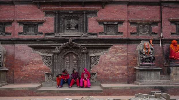 View of women sitting by a historic brick building in Nepal.