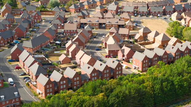 Aerial view of a modern residential housing estate with rows of red brick houses paved streets and surrounding green trees in Bedford England United Kingdom. Aerial view of a modern residential housing estate with rows of red brick houses paved streets and surrounding green trees in Bedford England United Kingdom.