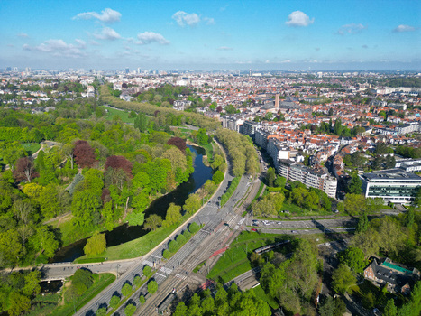 Aerial view of the lush green Parc de Woluwe with its winding lake adjacent to urban residential blocks and a tram line under a bright blue sky in Woluwe Saint Pierre Bruxelles Belgium. Aerial view of the lush green Parc de Woluwe with its winding lake adjacent to urban residential blocks and a tram line under a bright blue sky in Woluwe Saint Pierre Bruxelles Belgium.