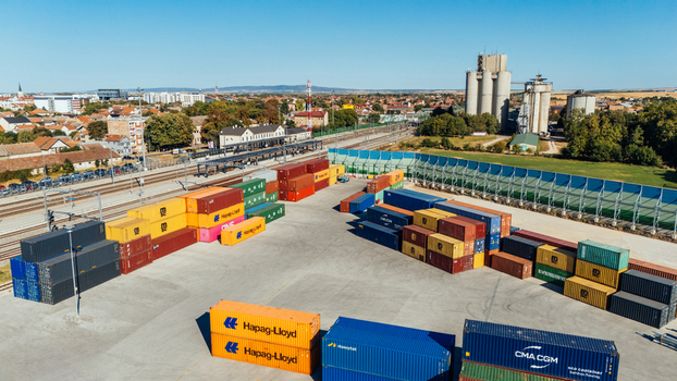 Indjija Vojvodina Serbia 24 August 2026 Aerial view of a logistics yard with colorful shipping containers adjacent railway tracks and industrial silos under a clear blue sky.