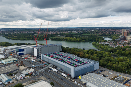 Aerial view of a data center under construction with colorful cooling units on the roof cranes and nearby river in the United Kingdom.