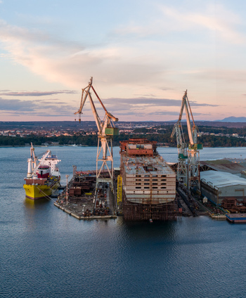 Aerial view of Uljanik Shipyard featuring large cranes a ship under construction and industrial buildings along the waterfront at sunset in Pula Croatia. Aerial view of Uljanik Shipyard featuring large cranes a ship under construction and industrial buildings along the waterfront at sunset in Pula Croatia.
