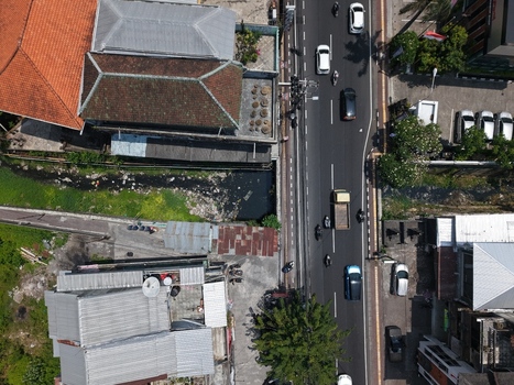 Aerial view of a busy road with cars and motorcycles adjacent to buildings with tiled roofs and a small canal in Kecamatan Denpasar Barat Bali Indonesia. Aerial view of a busy road with cars and motorcycles adjacent to buildings with tiled roofs and a small canal in Kecamatan Denpasar Barat Bali Indonesia.