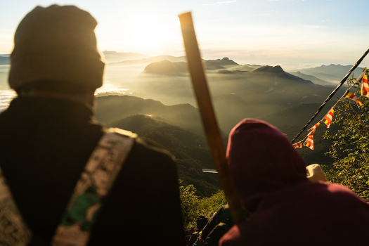 View of Adam s Peak at sunrise with people looking over misty mountain ranges and Buddhist prayer flags in Ratnapura Sabaragamuwa Province Sri Lanka. View of Adam s Peak at sunrise with people looking over misty mountain ranges and Buddhist prayer flags in Ratnapura Sabaragamuwa Province Sri Lanka.