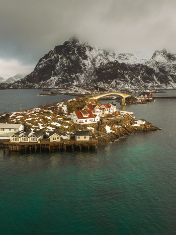 Aerial view of a quaint village nestled on a rocky island with snow dusted mountains rising dramatically in the background Henningsv&aelig;r Nordland Norway.