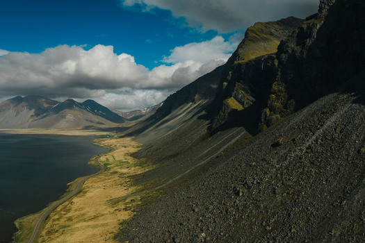 Aerial view of Stokksnes featuring dramatic mountains a winding coastal road and rugged terrain under a blue sky in Iceland.