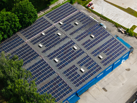Aerial view of a large industrial building roof covered with extensive solar panel arrays surrounded by green trees and a paved parking area in Riga Latvia. Aerial view of a large industrial building roof covered with extensive solar panel arrays surrounded by green trees and a paved parking area in Riga Latvia.
