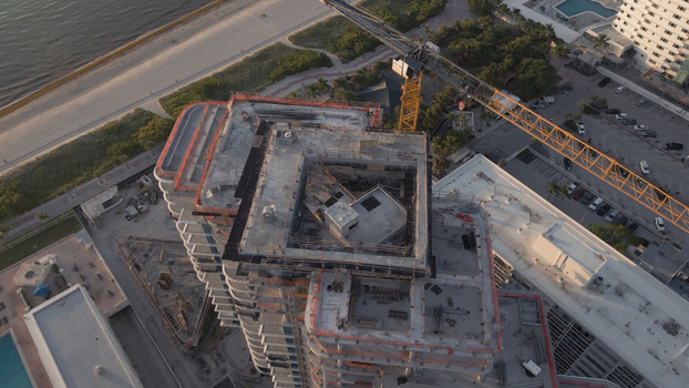 Aerial view of a high rise building under construction with a yellow crane adjacent parking lot and coastal scenery in Miami Beach Florida United States. Aerial view of a high rise building under construction with a yellow crane adjacent parking lot and coastal scenery in Miami Beach Florida United States.