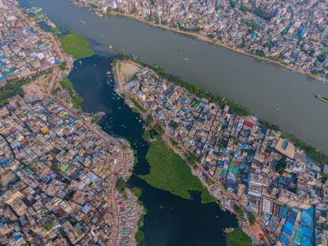 Aerial view of the Buriganga River flowing through the densely populated urban landscape with colorful rooftops and green water hyacinth in Keraniganj Dhaka Division Bangladesh. Aerial view of the Buriganga River flowing through the densely populated urban landscape with colorful rooftops and green water hyacinth in Keraniganj Dhaka Division Bangladesh.