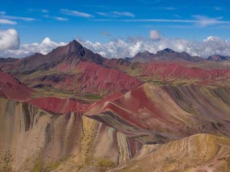 Aerial view of the colorful mineral rich slopes of Vinicunca Rainbow Mountain featuring vibrant red yellow and turquoise stripes under a bright blue sky in Cusco Cuzco Peru. Aerial view of the colorful mineral rich slopes of Vinicunca Rainbow Mountain featuring vibrant red yellow and turquoise stripes under a bright blue sky in Cusco Cuzco Peru.