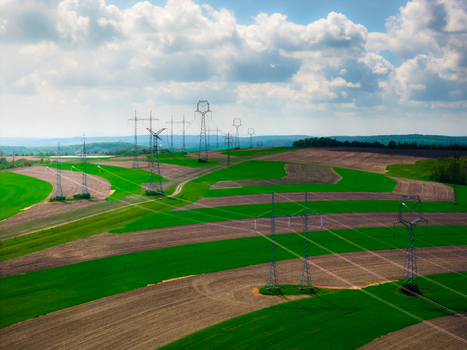 Aerial view of power lines crossing through vibrant green and brown agricultural fields under a cloudy sky in Brno South Moravian Region Czechia.