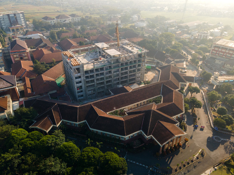 Aerial view of a large administrative complex featuring a building under construction surrounded by brown tiled roof buildings trees and roads in Banyumas Regency Central Java Indonesia.