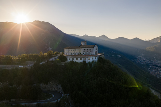 Aerial view of Santuario del Santissimo Salvatore perched on a mountain ridge with the sun setting behind peaks and a winding road below Montella Campania Italy. Aerial view of Santuario del Santissimo Salvatore perched on a mountain ridge with the sun setting behind peaks and a winding road below Montella Campania Italy.