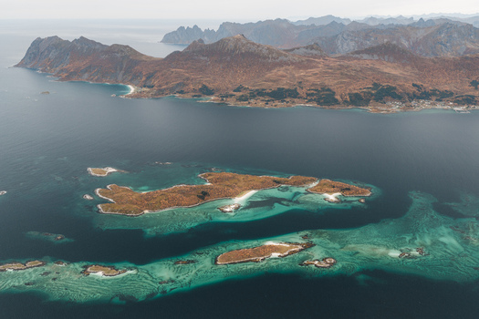 Aerial view of the rugged coastline and turquoise waters surrounding the island of Senja with dramatic mountain peaks in the background Senja Troms Norway.
