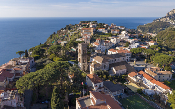 Aerial view of sunlight kissing the ancient Duomo di Ravello and the terracotta rooftops cascading down the hillside towards the azure sea Ravello Campania Italy. Aerial view of sunlight kissing the ancient Duomo di Ravello and the terracotta rooftops cascading down the hillside towards the azure sea Ravello Campania Italy.