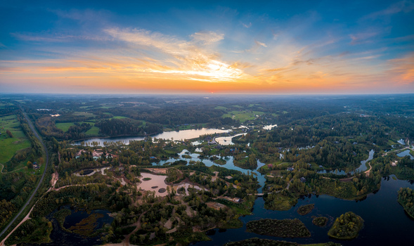 Aerial view of the lush Latvian landscape featuring winding rivers dense forests and scattered ponds under a vibrant sunset sky in Latvia. Aerial view of the lush Latvian landscape featuring winding rivers dense forests and scattered ponds under a vibrant sunset sky in Latvia.