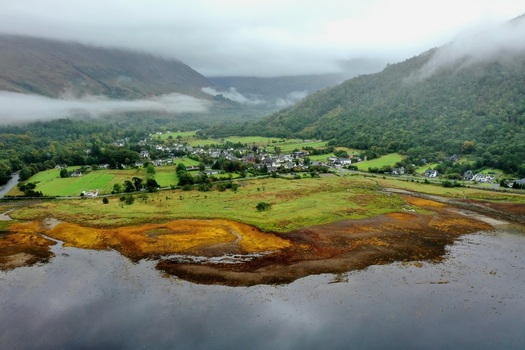 Aerial view of the village of Glencoe nestled in a lush green valley surrounded by misty mountains and water in Glencoe Scotland United Kingdom.