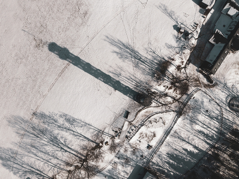 Aerial view of Majak Jary Cimrmana casting a long shadow over a snow covered landscape with nearby buildings and trees in Korenov Liberecky kraj Czechia. Aerial view of Majak Jary Cimrmana casting a long shadow over a snow covered landscape with nearby buildings and trees in Korenov Liberecky kraj Czechia.