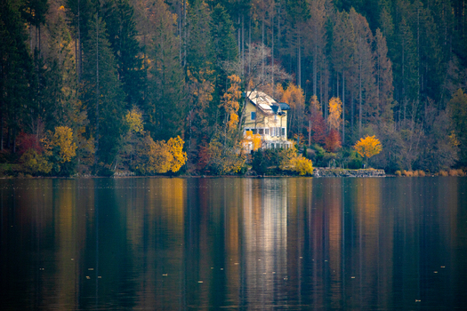 View of a yellow house nestled among colorful autumn trees reflected in the calm waters of a lake in Breitnau Baden Wurttemberg Germany. View of a yellow house nestled among colorful autumn trees reflected in the calm waters of a lake in Breitnau Baden Wurttemberg Germany.