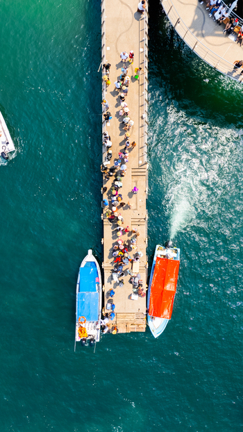 Aerial view of people lining the pier under the bright sun with boats docked on either side amidst the turquoise waters Puerto Vallarta Jalisco Mexico.